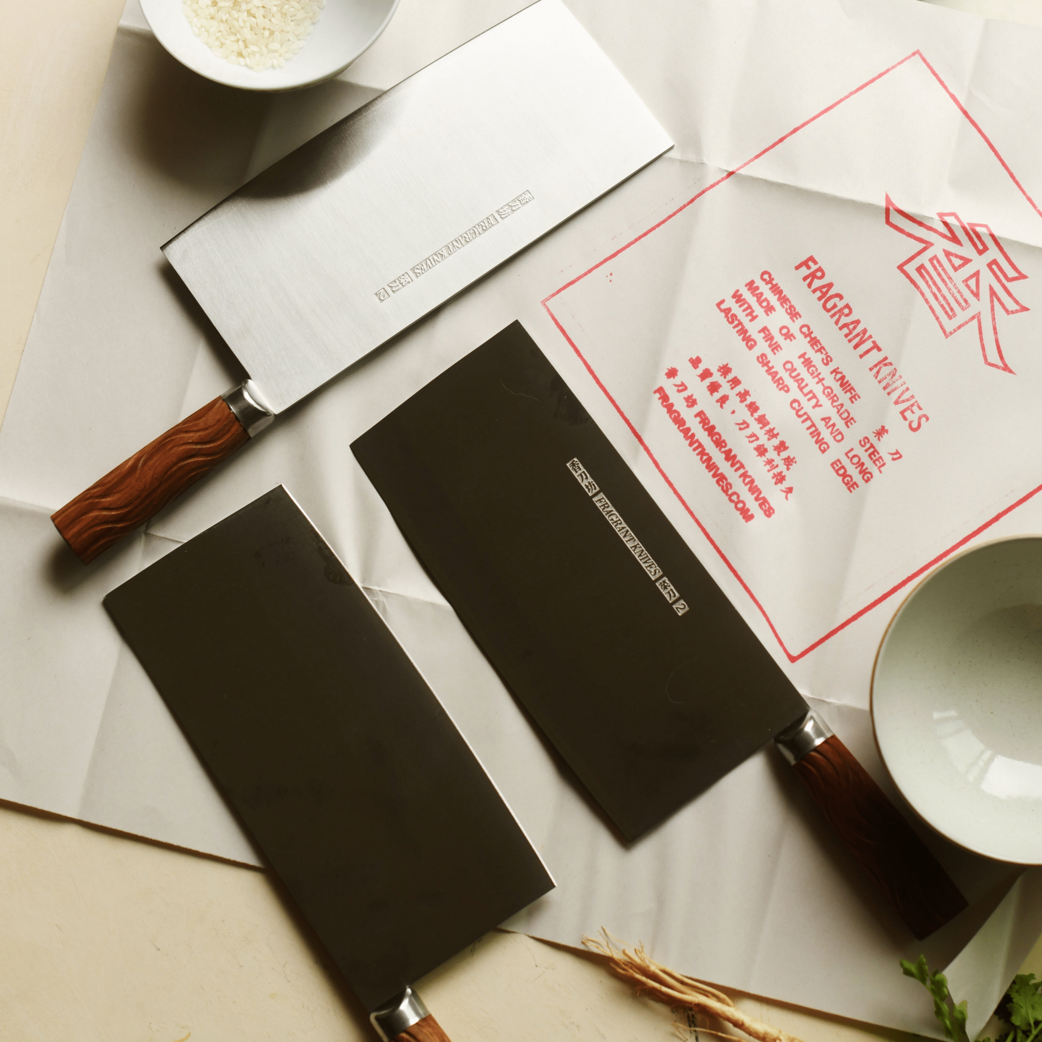 Two cleavers with rosewood handles on a surface with a 'Fragrant Knives' traditional branded Chinese knife paper.