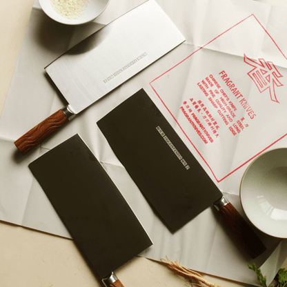 Two cleavers with rosewood handles on a surface with a 'Fragrant Knives' traditional branded Chinese knife paper.