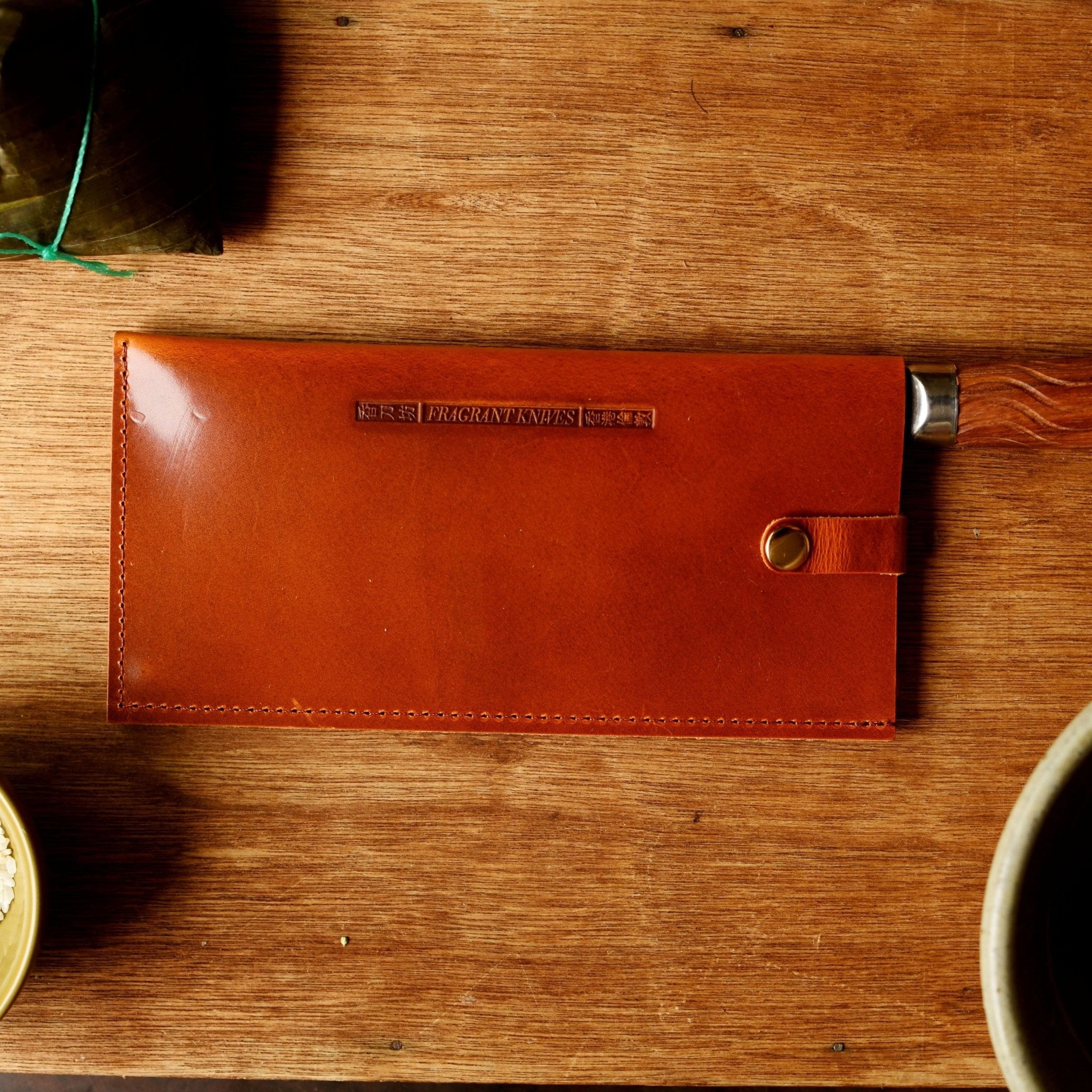 Brown leather knife sheath on a wooden surface with bowls of ingredients.